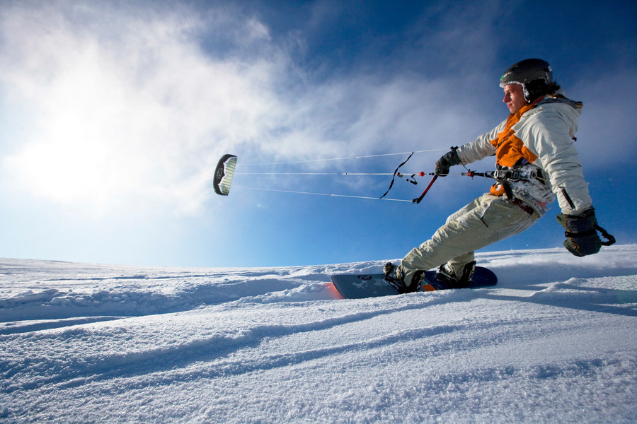 Eine Person steht auf einem Snowboard und lässt sich von einem Kite durch den Wind ziehen.